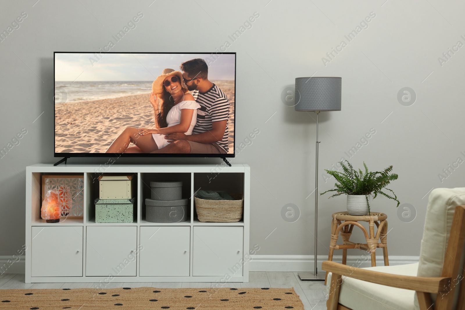 Image of Modern TV set on wooden stand in room. Scene of romantic movie on screen