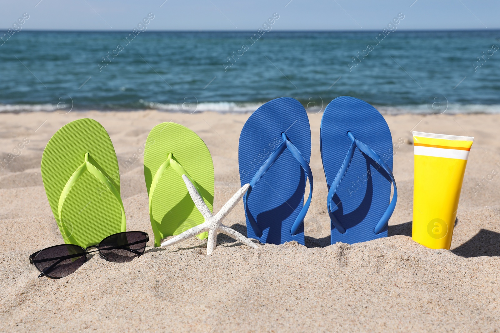 Photo of Stylish colorful flip flops, sunglasses and sunscreen on beach sand