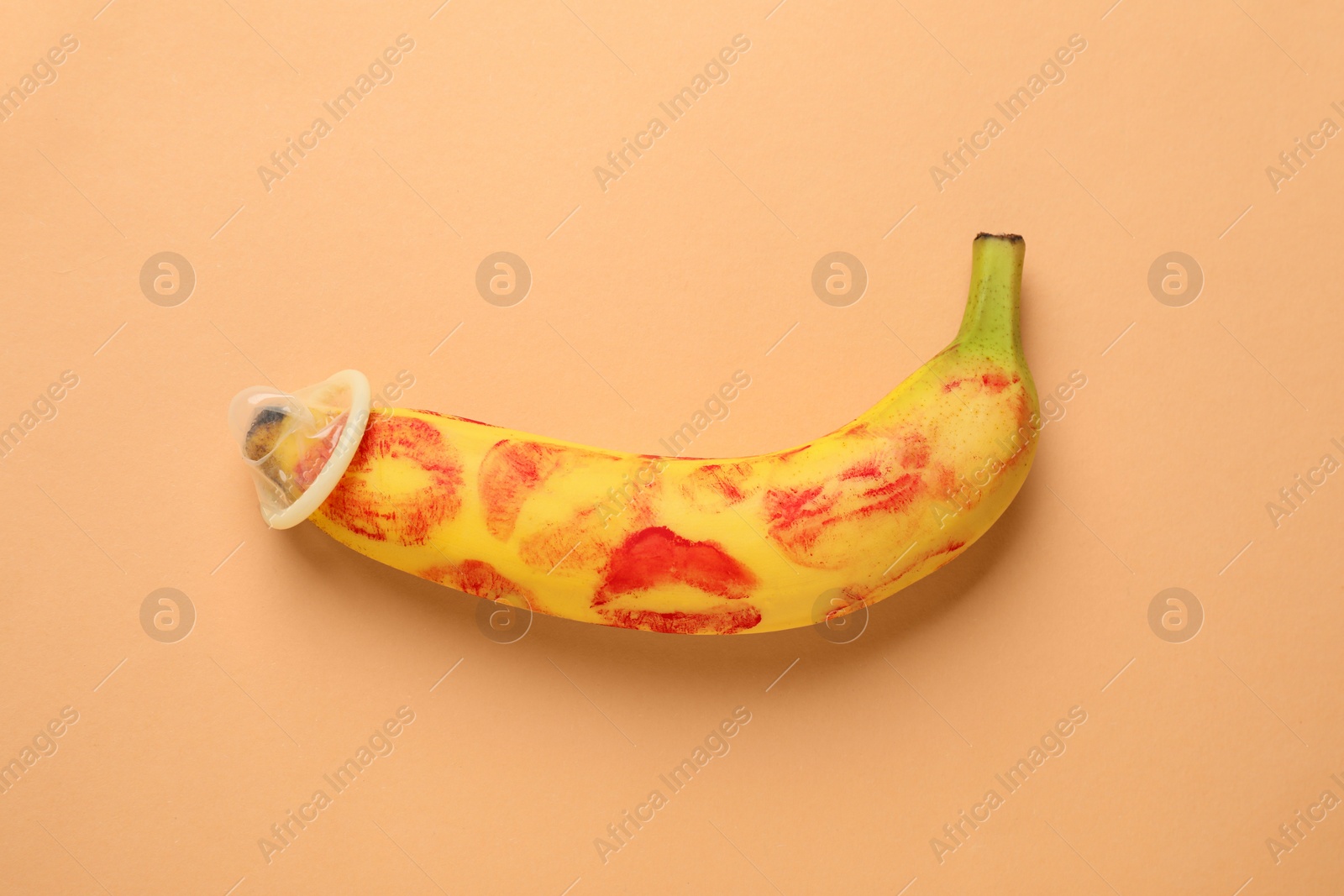 Photo of Banana with condom and red lipstick marks on pale orange background, top view. Safe sex concept