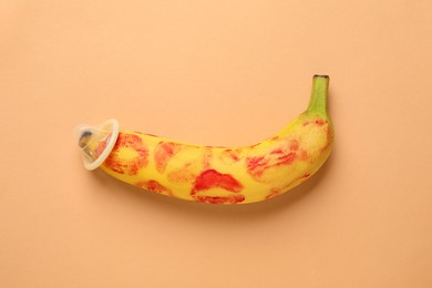 Photo of Banana with condom and red lipstick marks on pale orange background, top view. Safe sex concept