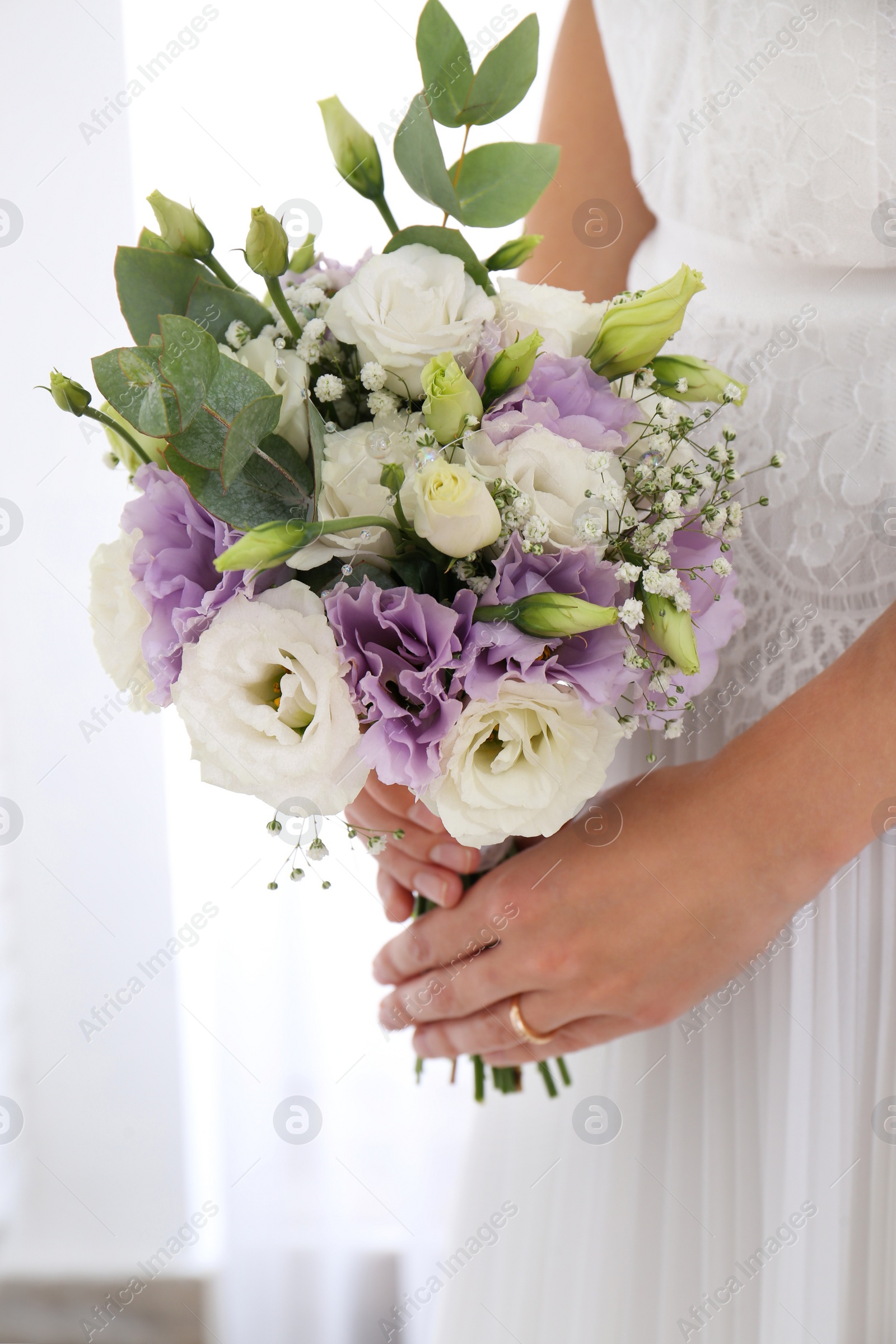 Photo of Bride holding beautiful bouquet with Eustoma flowers indoors, closeup