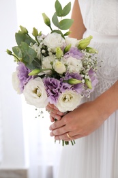 Bride holding beautiful bouquet with Eustoma flowers indoors, closeup