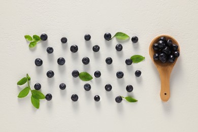 Tasty fresh bilberries, green leaves and spoon on white table, flat lay