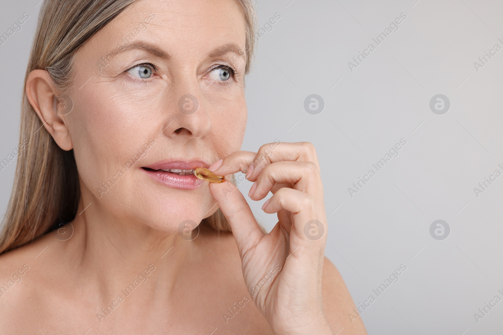 Photo of Beautiful woman taking vitamin capsule on grey background, space for text