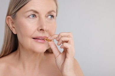 Photo of Beautiful woman taking vitamin capsule on grey background, space for text