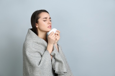 Photo of Young woman with blanket sneezing on light grey background, space for text. Runny nose