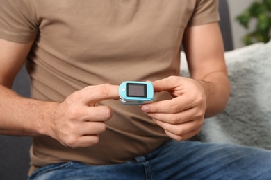 Man checking pulse with medical device at home, closeup