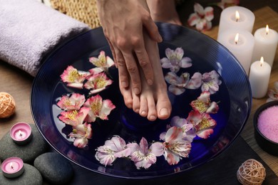 Photo of Woman putting her foot in bowl with water and flowers on floor, closeup. Spa treatment