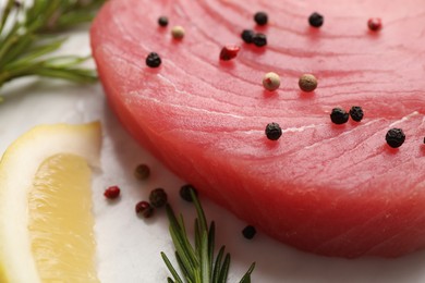 Photo of Raw tuna fillet with peppercorns, lemon and rosemary on white table, closeup