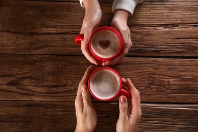 Photo of Women with mugs of hot coffee at wooden table, top view