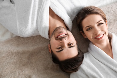 Photo of Happy young couple wearing bathrobes, top view. Visit to spa salon