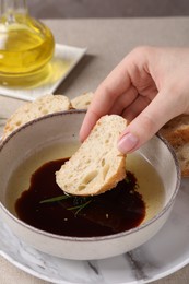 Woman dipping piece of bread into balsamic vinegar with oil and rosemary at table, closeup