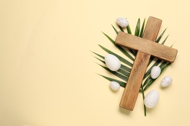 Wooden cross, painted Easter eggs and palm leaf on beige background, flat lay. Space for text