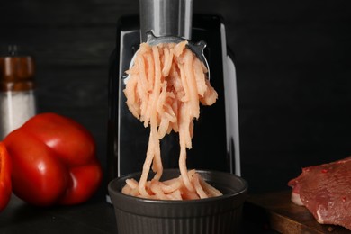 Photo of Electric meat grinder with chicken mince and products on black table, closeup