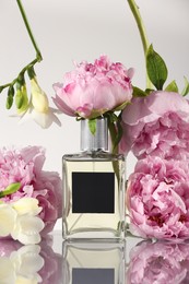 Bottle of luxury perfume and floral decor on mirror surface against light grey background