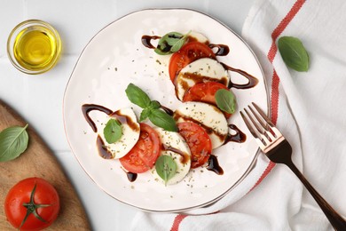 Photo of Delicious Caprese salad with balsamic vinegar served on white tiled table, flat lay