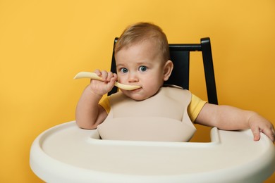 Photo of Cute little baby wearing bib while eating on yellow background