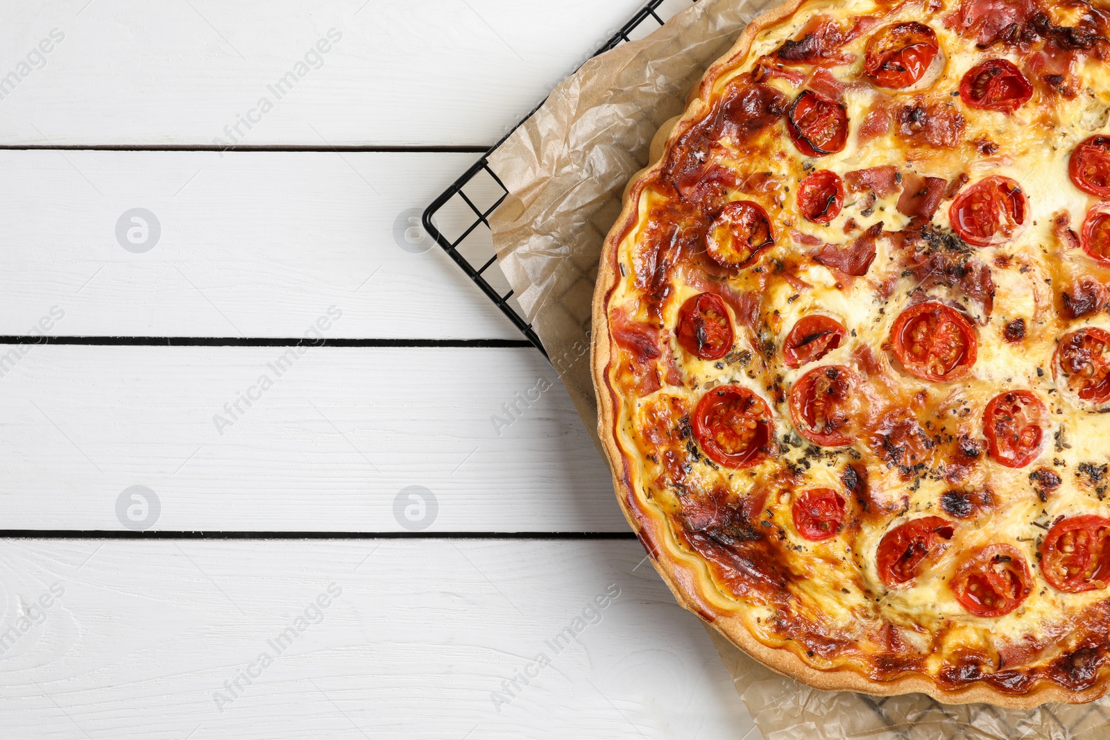 Photo of Delicious homemade quiche with prosciutto and tomatoes on white wooden table, top view. Space for text