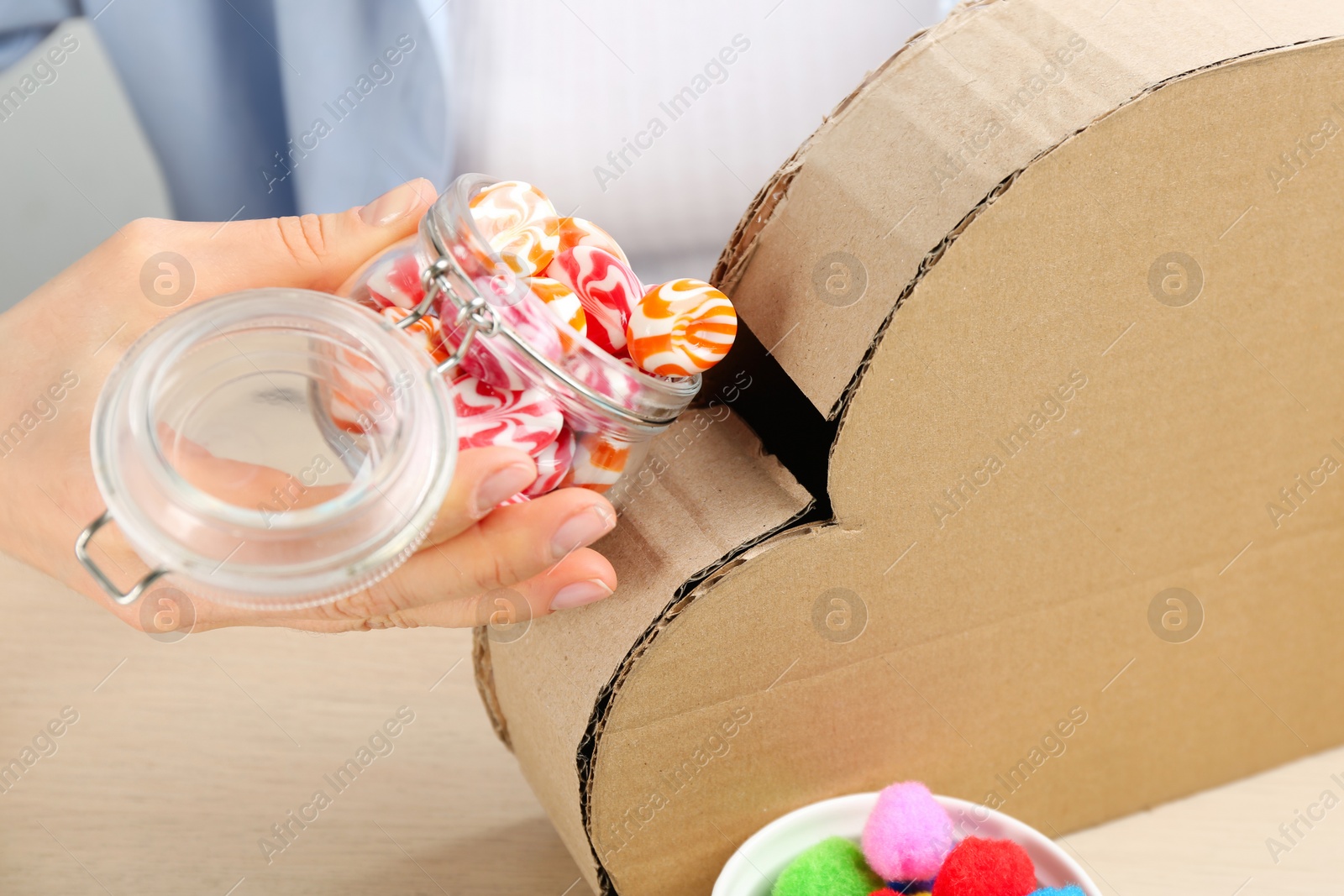 Photo of Woman putting candies into cardboard cloud at wooden table, closeup. Pinata diy