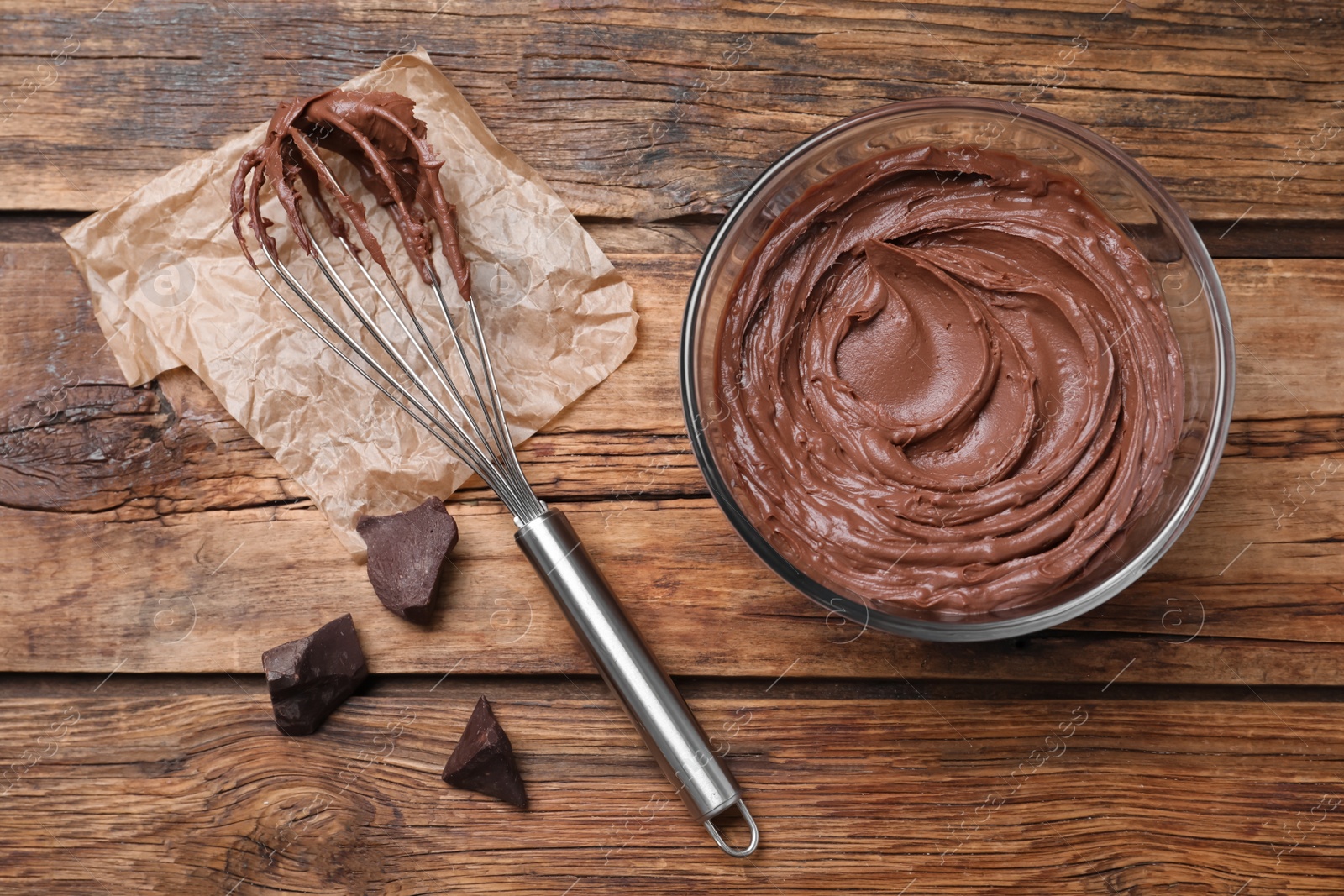 Photo of Chocolate cream and balloon whisk on wooden table, flat lay