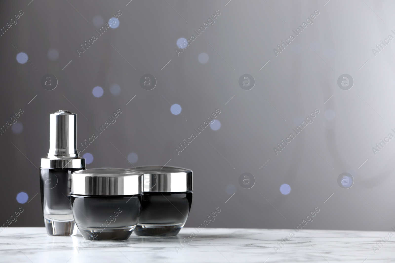 Photo of Skin care products on white marble table against blurred lights, space for text