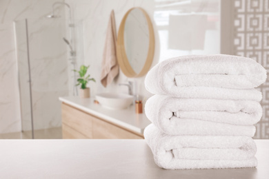 Stack of fresh towels on light grey table in bathroom. Space for text