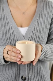 Photo of Woman holding burning soy candle in ceramic holder, closeup