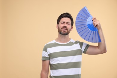 Photo of Unhappy man with hand fan suffering from heat on beige background. Space for text