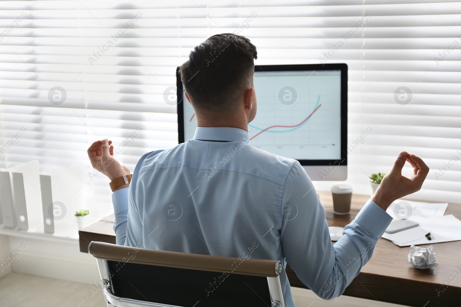 Photo of Businessman meditating at workplace in office, back view. Stress relieving exercise