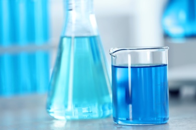 Beaker with light blue liquid on table in laboratory. Space for text