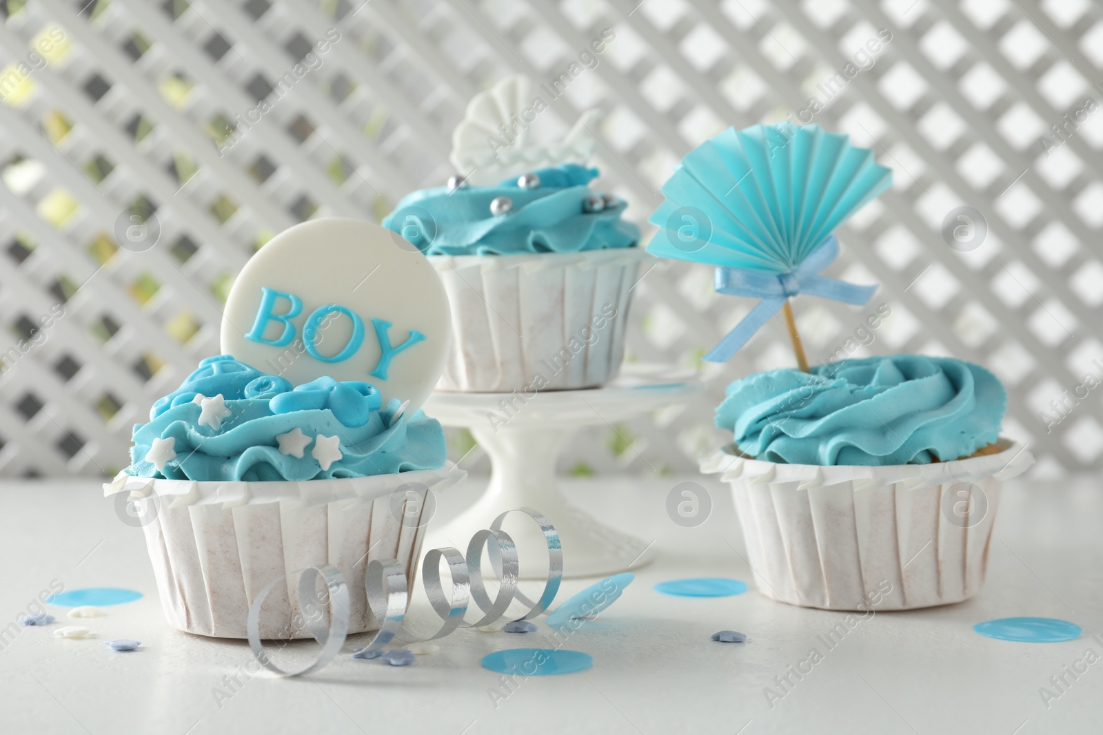 Photo of Delicious cupcakes with light blue cream and toppers for baby shower on white table