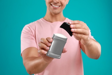 Young man holding deodorant on blue background, closeup. Mockup for design