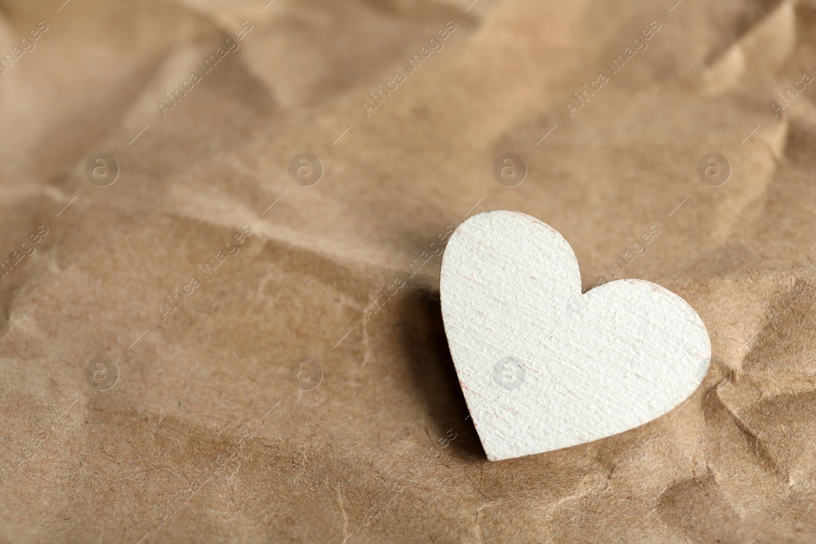 Photo of White wooden heart on crumpled kraft paper, space for text. St. Valentine's day