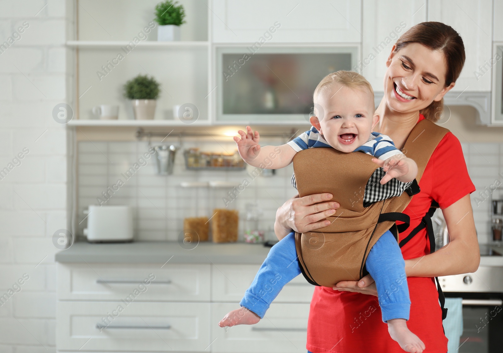 Photo of Woman with her son in baby carrier at home. Space for text