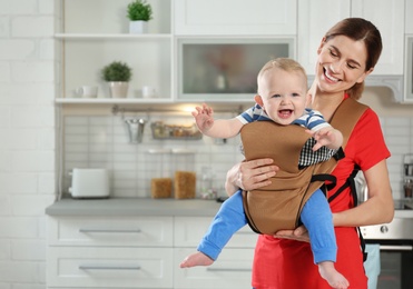 Photo of Woman with her son in baby carrier at home. Space for text