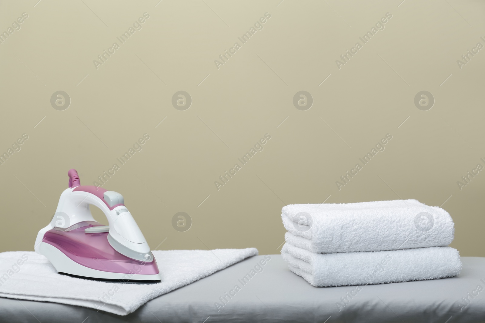 Photo of Modern iron and clean towels on board against beige background. Space for text