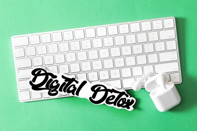 Photo of Computer keyboard, earphones and paper with words DIGITAL DETOX on green background, flat lay