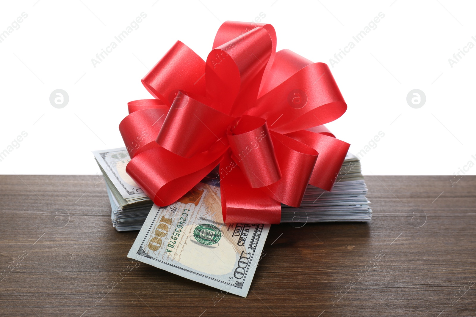 Stack of dollar bills with red bow on wooden table against white background Photo of Stack of dollar bills with red bow on wooden table against white background