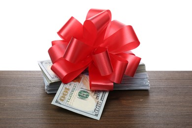 Photo of Stack of dollar bills with red bow on wooden table against white background