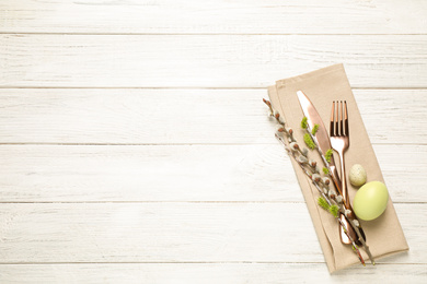 Photo of Cutlery set and beautiful willow branches on white wooden table, top view with space for text. Easter celebration