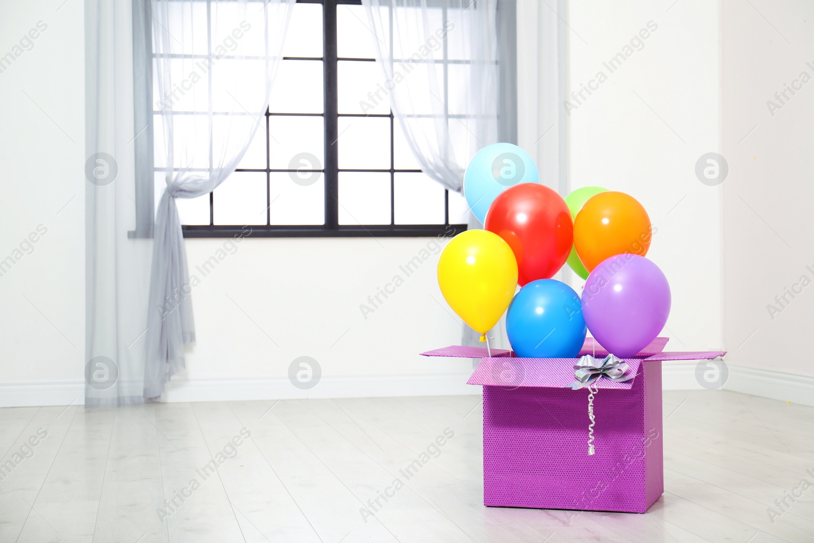 Photo of Gift box with bright air balloons on floor indoors. Space for text