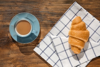 Photo of Fresh croissant and cup of coffee on wooden background, top view