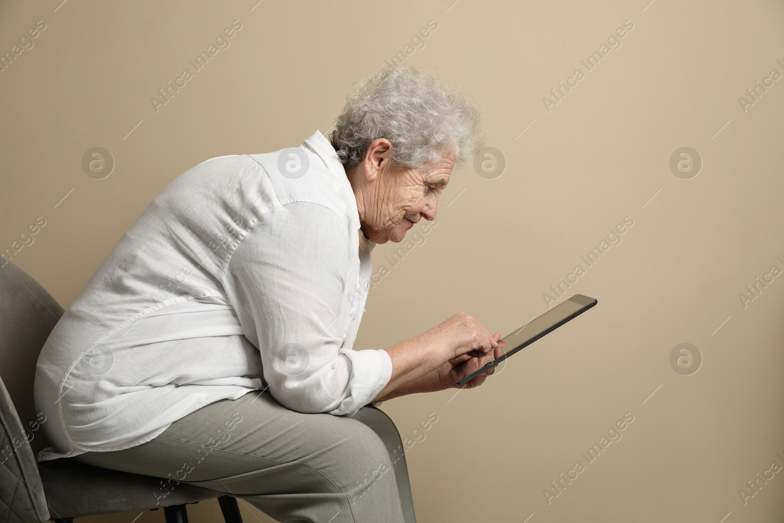 Photo of Elderly woman with poor posture using tablet on beige background