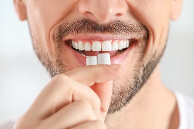 Photo of Man putting chewing gums into mouth on light background, closeup