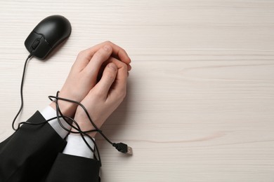 Photo of Man showing hands tied with computer mouse cable at white wooden table, top view. Internet addiction