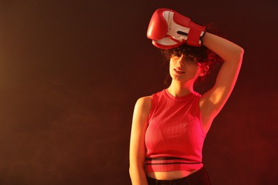 Photo of Beautiful young woman with boxing gloves on color background in neon lights and smoke. Space for text