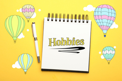 Image of Notebook with word Hobbies and pen on yellow background, top view