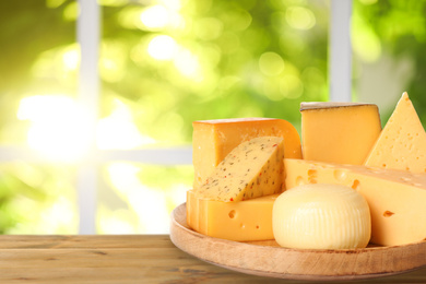 Different types of delicious cheeses on wooden table outdoors, space for text. Dairy products