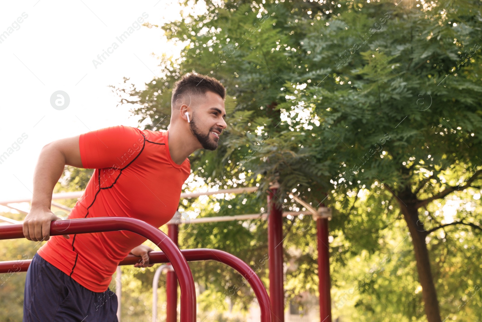 Photo of Young man with wireless headphones listening to music while exercising on sports ground. Space for text