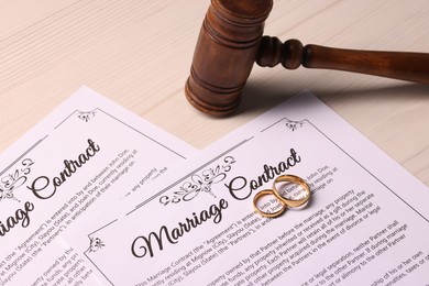 Marriage contracts, gold rings and gavel on light wooden table, closeup